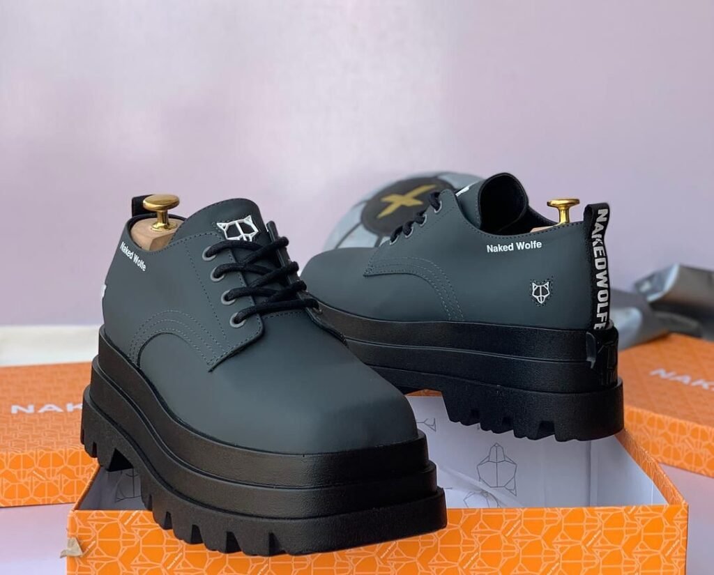 Naked Wolf Loafer in a stylish, black color with a platform sole and thick midsoles. The brand's logo and tagline are prominently displayed on the side. The shoe is shown in a box, ready for purchase.